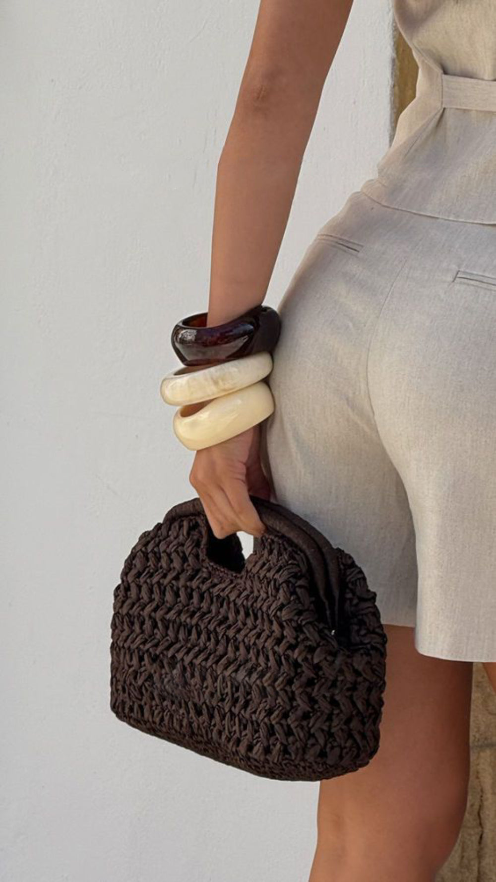 hand holding dark brown crochet clutch bag resin bangles linen shorts wall - brown - clutch bag