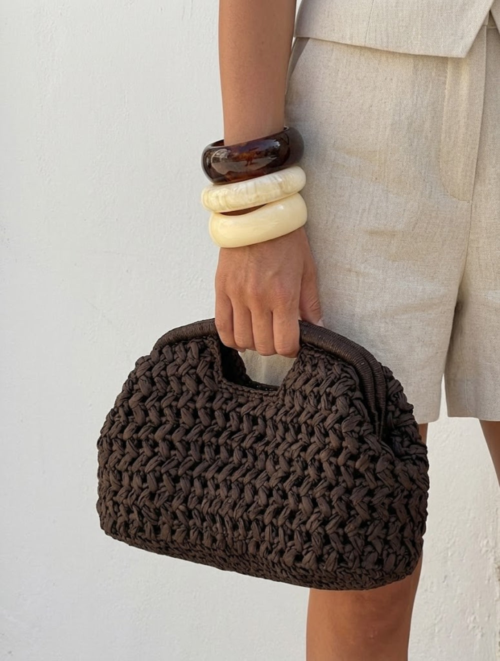 woman hand gripping brown crochet clutch bag resin bangles linen shorts - brown - clutch bag